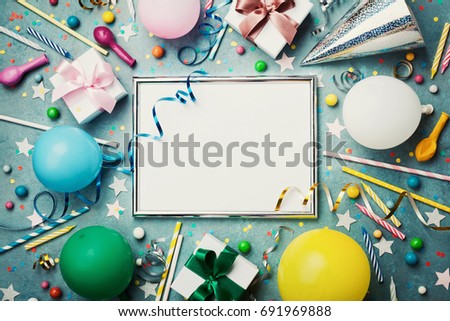 Party or birthday background. Silver frame with colorful balloon, gift box, carnival cap, confetti, candy and streamer on vintage blue table top view. Flat lay style. Holiday mockup.