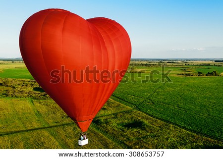 Red balloon in the form of heart over green fields and forests