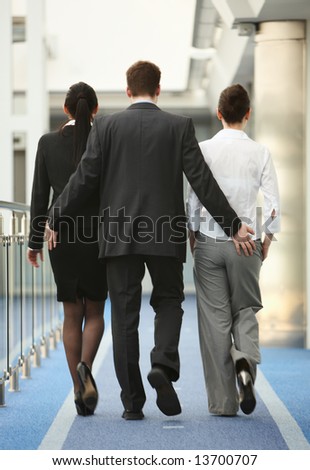 Business portrait of tree persons - young man and two women being touched by a man in modern office corridor