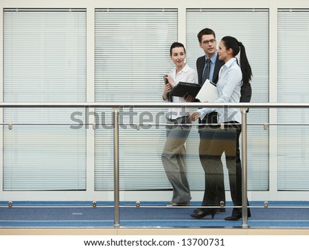 Business portrait of tree presons - young man and two women having nice chat talk on modern office corridor