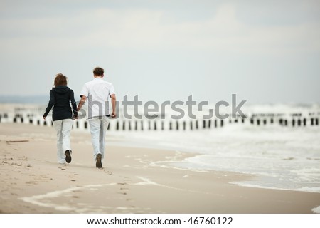 two young people runnig on the beach kissing and holding tight