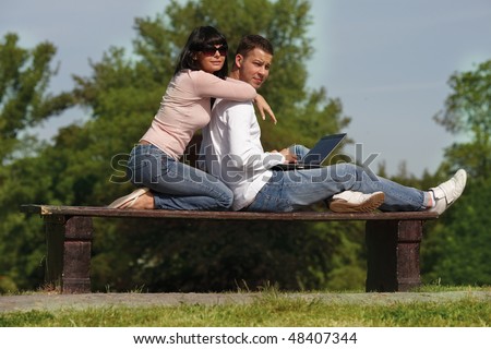 couple in park sitting together on bench working reading computer