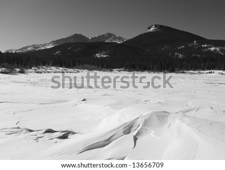 Mountain peaks overlook drifting snow on a frozen lake.