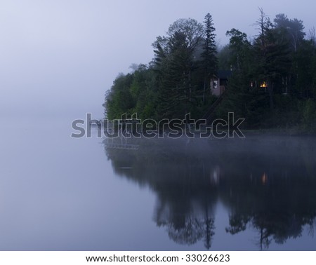 Glow from a cabin window in a morning fog on Island Lake in Northern Minnesota