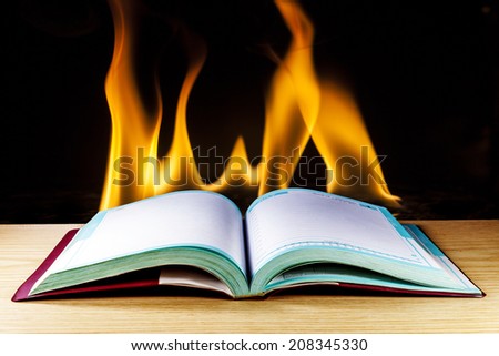 Open book on wood table over Fire flames background