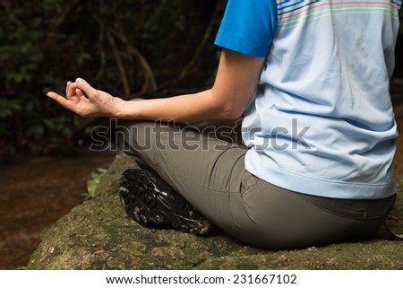 Woman meditates in the nature, next to a stream