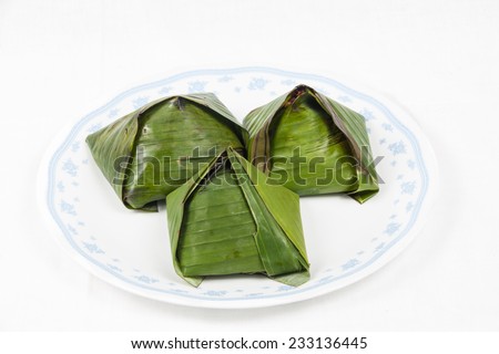 Three unopened simple and authentic nasi lemak that is wrapped in banana leaf served on a plate