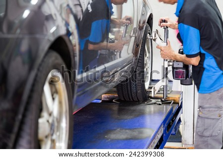 Mechanic fixing the wheel alignment device onto a car wheel. Focus is on the car wheel and wheel alignment device.