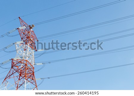 Red and white electricity pylon against blue sky