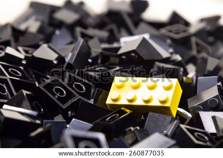 Pile of black color building blocks with selective focus and highlight on one particular yellow block using available light