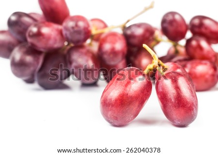 Focus on three pieces of crimson red grapes on foreground and with de-focused bunches of grapes at the background