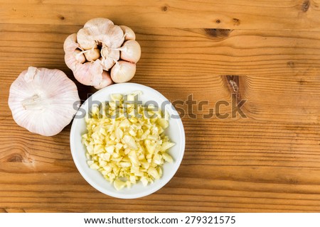 Chopped garlic in a plate with garlic bulbs on wooden table