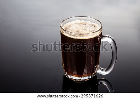Aromatic hot black coffee in transparent glass against dark background