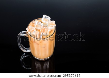 Refreshing ice cold tea with milk in transparent glass from elevated angle against dark background