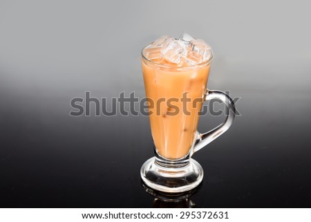 Refreshing ice cold tea with milk in transparent glass against dual tone background