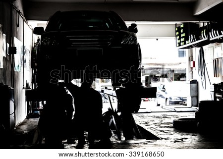 Silhouette image of mechanics inspecting cars suspended on platform in a very small and tight workshop