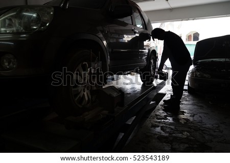 Silhouette of mechanic fixing car aligner onto car wheel in workshop garage