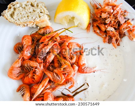 pink shrimps with sauce, bread, lemon served on a white plate.