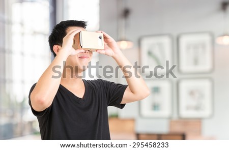 A asian man holding cardboard virtual reality goggle on background.