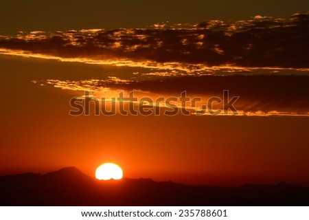 Sun setting below clouds on mountain horizon