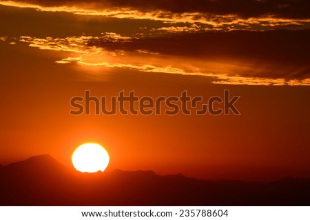 Sun setting below clouds on mountain horizon