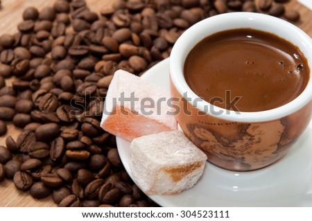 A cup of coffee and Turkish delight on a wooden board and raw coffee beans.