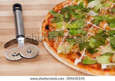 Pizza with lettuce and pizza cutter on the wooden board.