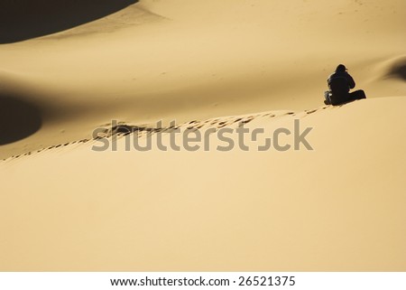 Silhouette of a person seat alone in the dune desert, Morocco