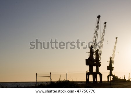 Group of huge sky cranes at a construction site at sunset, silhouette against orange sky
