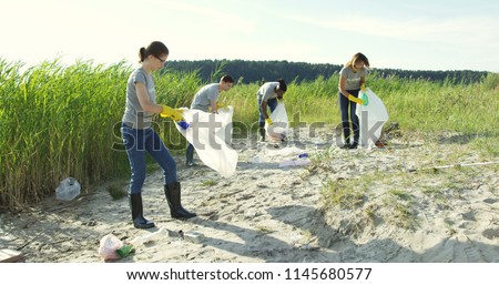 Group of young volunteers helping to keep nature clean and picking up the garbage from a sandy shore.