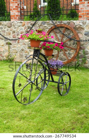 Decorative metal bicycle with flowers on green grass on a background of stone wall