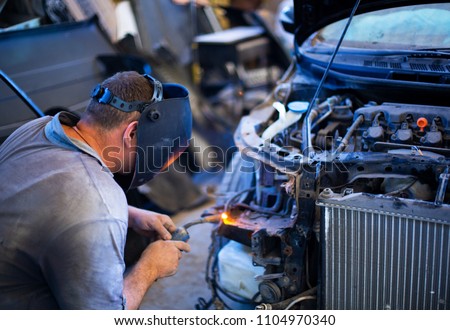 Welding industrial: worker in helmet repair detail in car auto service