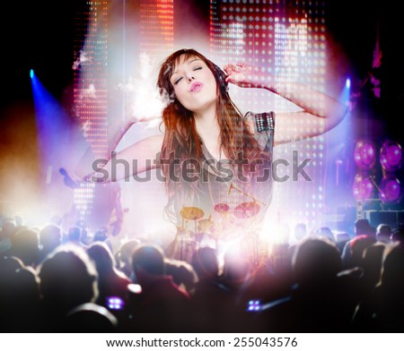 Beautiful woman listening to music with headphones and silhouettes of concert crowd in front of bright stage lights. Concept background of live music and party