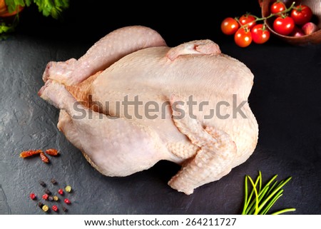 Raw meat. Whole raw chicken on black stone with tomato