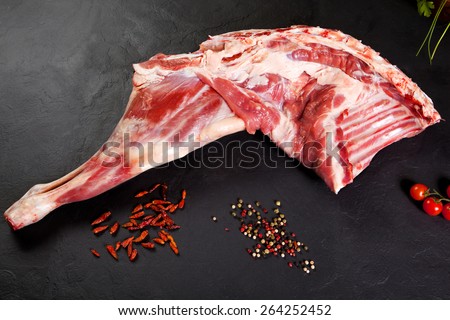 Fresh and raw meat. Raw lamb leg on black background with tomato and pepper