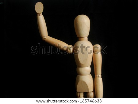 Wooden dummy man waving hello on black background