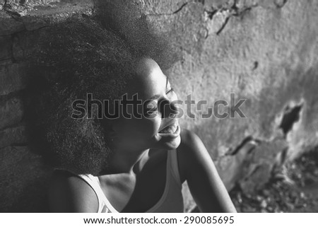 young happy and  pretty curly afro woman laughing and sitting near old wall. black and white picture