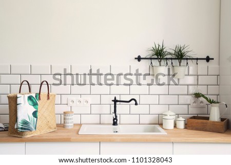 Modern and design scandinavian kitchen with plants, accessories and straw bag.  Sunny and bright space with white brick wall.
