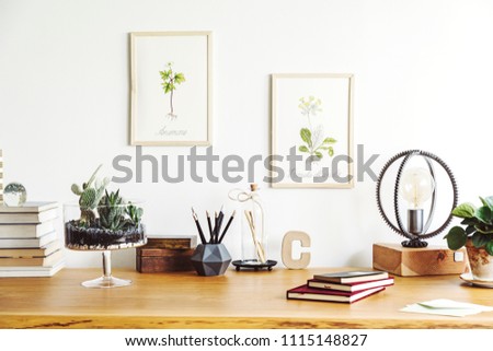 Vintage, creative home office interior with wooden desk, books, notebooks, romantic illustrations of plants, table lamp and office accessories. Stylish space for freelancer.