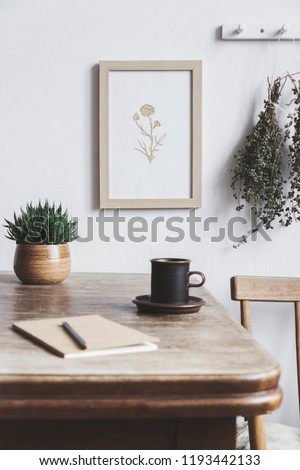 Stylish interior design of kitchen space with small table with mock up frame, herbs, cups of tea and notebooks. Minimalistic interior.