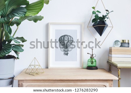 The room interior with mock up photo frame on the retro wooden shelf. Hanging plant in design pot, tropical plant, gold pyramid, design coffe table with books. Concept of minimalistic retro shelf.