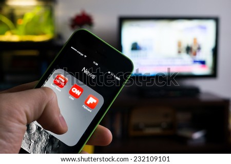 BUCHAREST, ROMANIA - NOVEMBER 21, 2014: Photo of hand holding an iphone with news apps on screen and tv set in the background with news channel