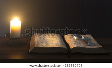 Book and candle on the table on a dark background