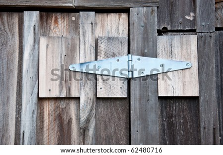 A new door hinge repairing an old barn door with natural, rough-hewn lumber