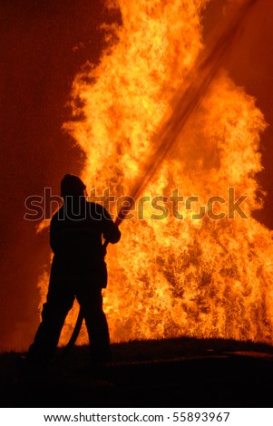 lone fireman battling against raging fire, NOTE: shallow focus on material burning in fire, top left corner particles from water spray, not camera noise