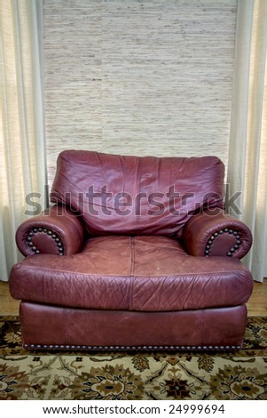 Comfortable red leather seat in a room in between two windows.