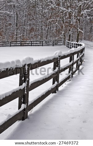 Snow covered wooden fence line that borders a field.