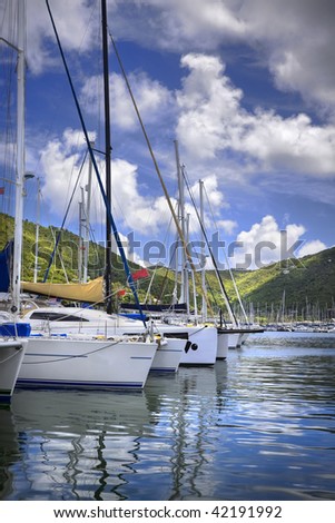 Beautiful tropical harbor lined with sailboat yachts and lush mountains in the background.