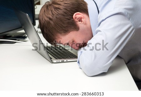 Young handsome man with computer in the office. Thinking over task in programming. Speeping upon a laptop keyboard