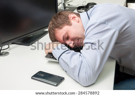 Young handsome man with computer in the office. Thinking over task in programming. Sleeping upon a keyboard